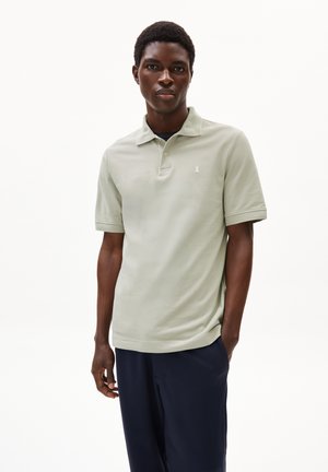 Lichtgroene polo met kraag, witte logodetail op de linkerkant van de borst, gladde stof, gecombineerd met donkerblauwe broek.