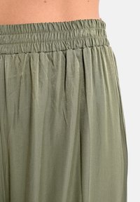 Pantaloni in tessuto leggero e verde con vita elasticizzata. Presentano una texture morbida e pieghe verticali per un design fluido.
