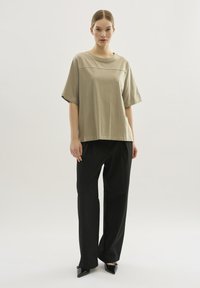Camiseta de algodón de corte suelto y manga corta en beige claro con cuello redondo, combinada con pantalones negros de cintura alta y zapatos negros de punta.