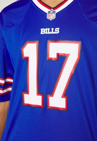 Camisa da NFL azul com detalhes vermelhos. Exibe "BILLS" em texto branco e o número "17" em branco contornado por vermelho e preto. Mangas curtas.