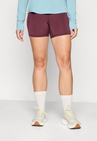 Angepasste kastanienbraune Sportshorts kombiniert mit einem hellblauen Langarmoberteil, ergänzt durch weiße Crew-Socken und helle Sneakers mit einer Gummisohle.