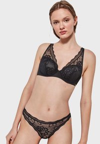 Reggiseno in pizzo nero e perizoma abbinato, caratterizzati da intricati motivi floreali, scollatura profonda e bordi scallopati. Texture morbida e delicata.