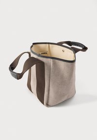 Καμβάς τσάντας με δομημένο σχήμα, διαθέτει ανοιχτό καφέ και σκούρο καφέ ρίγες, μαύρη περιθώριο και δύο κοντούς χειρολαβές. Το εσωτερικό είναι μπεζ.