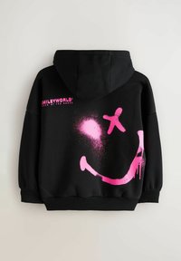 Mustahuppari, jonka selässä on vaaleanpunaisella spraymaalilla tehty hymyilevän naaman kuvio ja yläpuolella teksti "SMILEYWORLD! by TED BAKER". Pehmeä kangas, rento istuvuus.