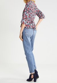 Top peplum floreale con maniche a campana, abbinato a jeans dritti blu chiaro e tacchi a caviglia blu navy. Tessuto testurizzato e dettaglio con fiocco visibili.