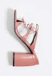 Sandale à talon carré rose brillant avec trois brides nouées en nœuds sur fond blanc.