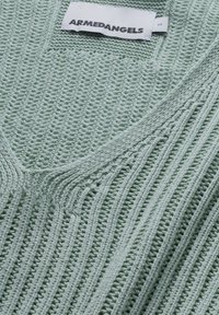 Vêtement tricoté vert clair avec texture côtelée et étiquette blanche cousue indiquant ARMEDANGELS et taille S.