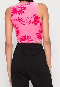Kvinna i en rosa ärmlös crop top med röda blommönster och svarta högmidjade byxor, sedd bakifrån.