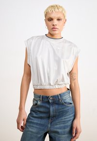 White cropped t-shirt with a gathered hem, short sleeves, and subtle stripe pattern. Paired with high-waisted blue denim jeans.