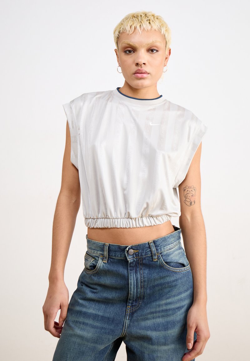 White cropped t-shirt with a gathered hem, short sleeves, and subtle stripe pattern. Paired with high-waisted blue denim jeans.