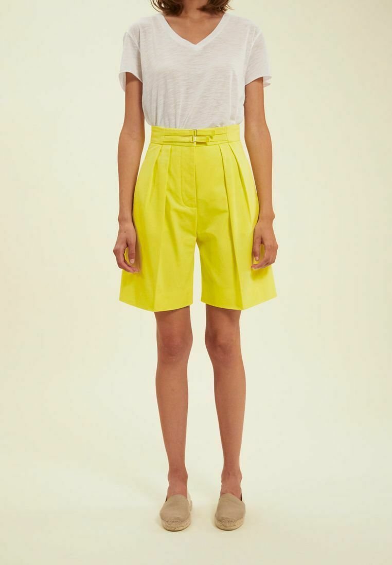 Shorts jaunes taille haute avec des plis, en matière légère. Associés à un t-shirt blanc à col en V et des espadrilles beiges.