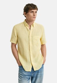 Kurzärmeliges, einfarbiges Hemd aus hellgelbem Leinen mit einer Brusttasche. Verfügt über einen Kragen und einen lässigen Schnitt. Kombiniert mit hellblauen Jeans.