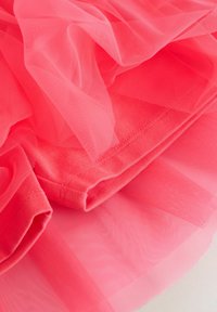 Tela de tul color coral con una capa superpuesta y una capa inferior lisa y sólida. El tul es suave y ligeramente translúcido, creando un efecto voluminoso.