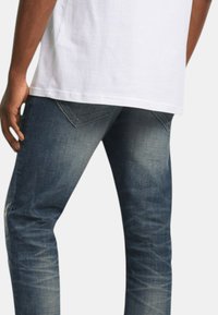 Jeans in denim blu con una finitura leggermente sbiadita, design a cinque tasche e vestibilità a vita media. Cuciture visibili e superficie del tessuto testurizzata.