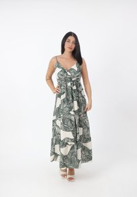 Abito lungo con motivo foglia verde su sfondo beige chiaro. Presenta spalline regolabili e vita arricciata, realizzato in un tessuto leggero.