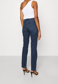 Vaqueros de mezclilla de lavado oscuro con una forma entallada y alta cintura, acompañados de una blusa blanca de un solo hombro y tacones de aguja negros.