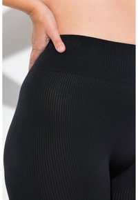 Leggings noirs côtelés avec une large ceinture, présentant un motif texturé et une coupe ajustée. Le tissu semble doux et extensible.