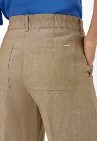 Lichtbruine linnen broek met een gestructureerde afwerking, voorzien van twee achterzakken en een klein metalen label op de tailleband.