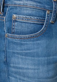 Blå denimjeans med en klassisk femficksdesign, whisker-textur, kopparstygn och metallhårdvara på bakfickan.