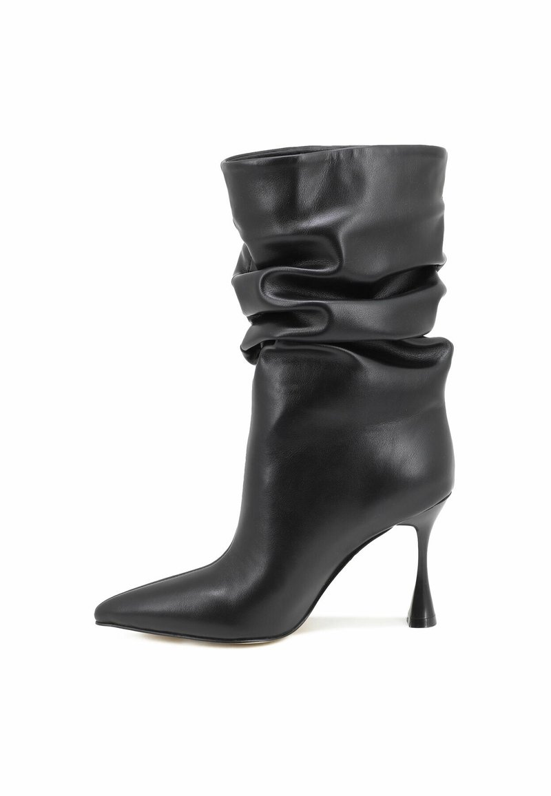 Botte molle en cuir noir mi-mollet avec bout pointu et talon haut évasé sur fond blanc.