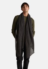 Černý, texturovaný šátek volně draped kolem krku, vyrobený z měkké látky s mírně třásněním na okrajích, doplňující zelený top s dlouhým rukávem.