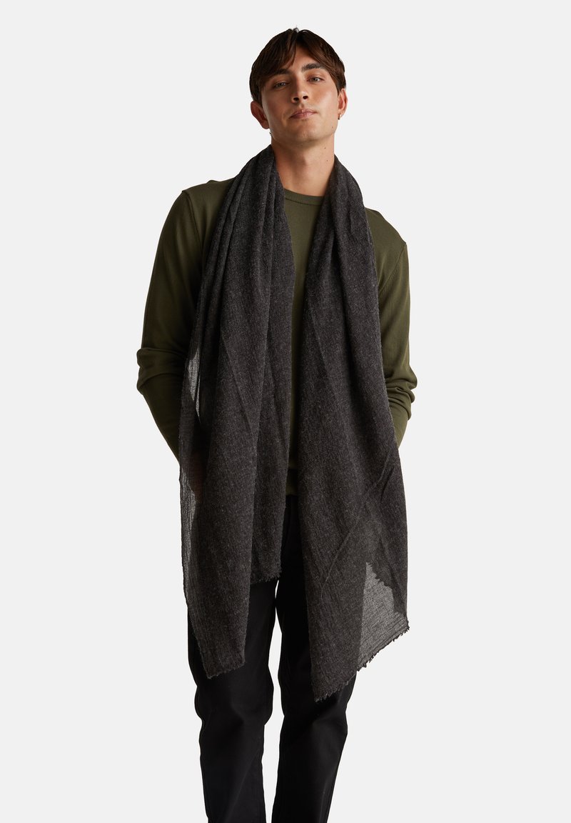 Černý, texturovaný šátek volně draped kolem krku, vyrobený z měkké látky s mírně třásněním na okrajích, doplňující zelený top s dlouhým rukávem.