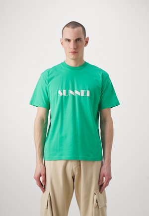 Green cotton t-shirt with short sleeves, featuring the word "SUNNEI" in white letters across the chest. Simple, unadorned design.