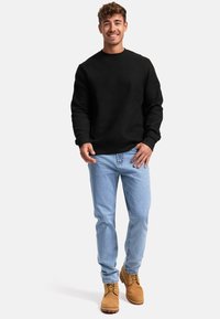 Felpa nera a trama con scollatura rotonda, jeans azzurri e stivali da lavoro beige. Design semplice, vestibilità dritta e dettagli minimi.