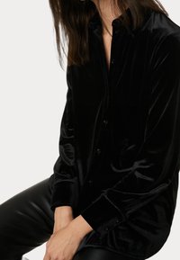 Czarna aksamitna koszula zapinana na guziki z kołnierzykiem, długimi rękawami i luźnym krojem. Charakteryzuje się gładką fakturą i subtelnym połyskiem.