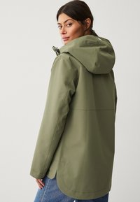 Chaqueta impermeable verde oliva con capucha, que presenta una textura suave, un cordón elástico en el escote y un dobladillo curvado.