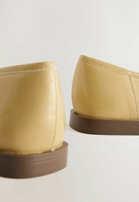 Geel leren schoenen met een gladde textuur, met een ronde vorm en een bruine rubberen zool. Stikdetails zijn zichtbaar langs de randen.