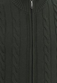 Donkergroene gebreide cardigan met een hoge kraag, voorzien van kabelbreipatronen en een voorrits met een zwart trekkoordje.