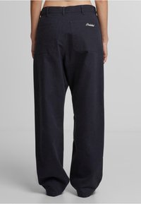 Pantalones de corte amplio en azul oscuro, confeccionados con algodón de textura suave. Presentan dos bolsillos traseros y un bordado sutil de "Prohibido".