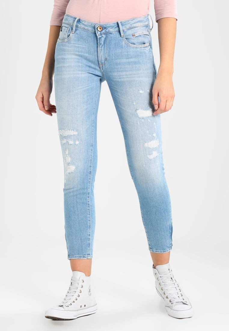 Lichtblauwe, versleten denim jeans met een subtiele vervaging, slim fit, vijf pockets ontwerp en een knoopsluiting. Gecombineerd met witte sneakers.