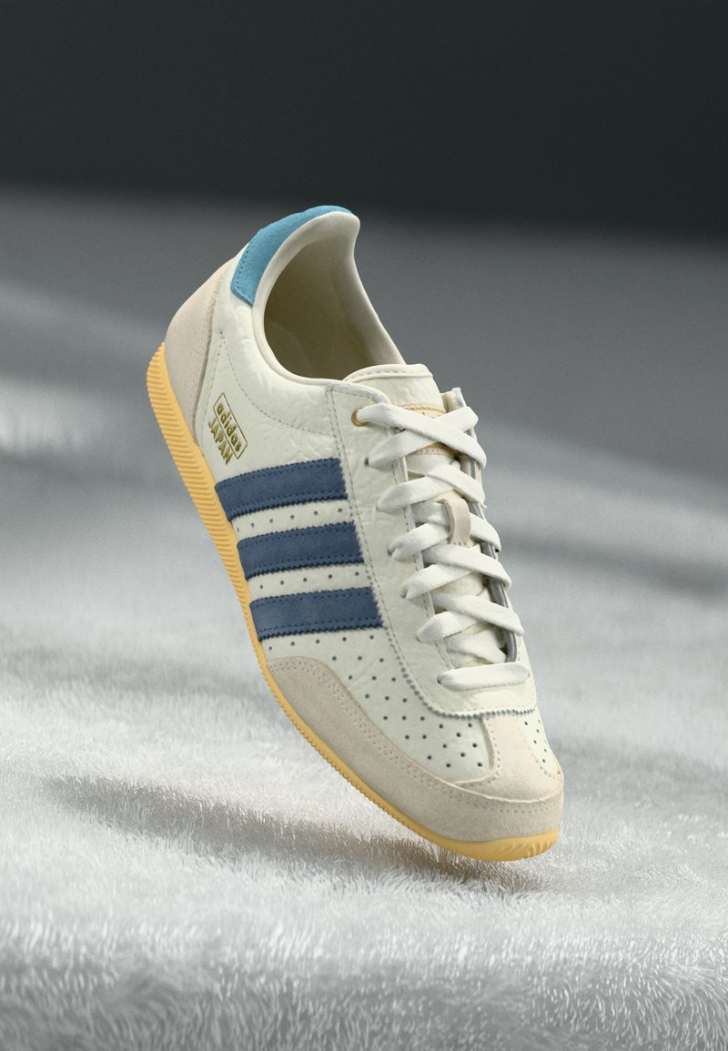 Valkoiset Adidas Japan -kengät, joissa on siniset raidat, vaaleansininen kantapääpätkä, beigen väriset mokkahighit ja keltainen pohja teksturoidulla valkoisella pinnalla.