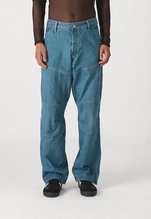 Light blue denim pants with a loose fit, featuring patchwork detailing and multiple seams. Paired with black sneakers.