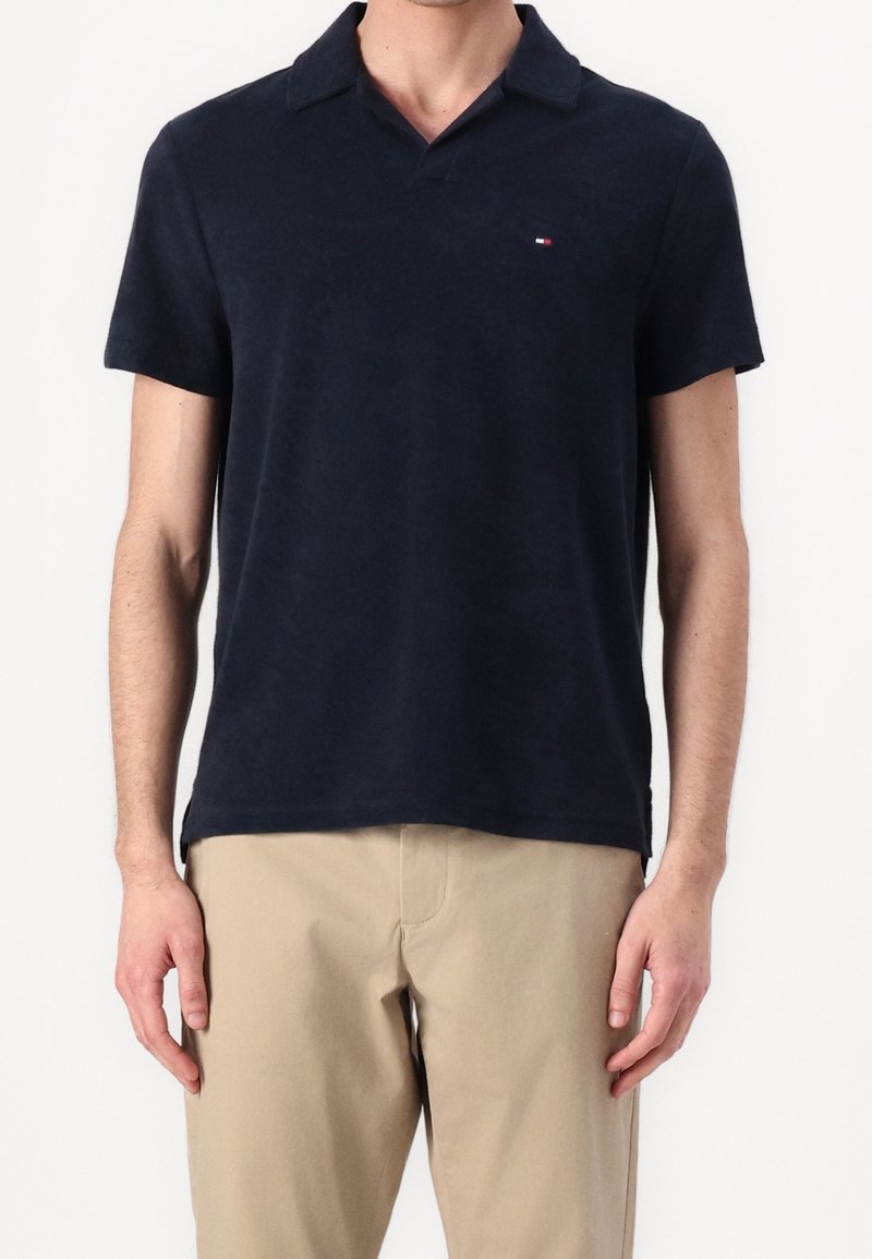 Polo en coton de couleur marine, avec un col classique, des manches courtes et un petit logo de la marque sur la poitrine. Texture lisse.