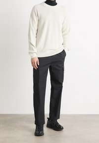 Krémový žebrovaný svetr, černé cargo kalhoty s bočními kapsami a černé tenisky. Minimalistický design, texturovaný materiál, pohodlný střih.