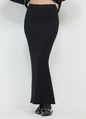 Gonna lunga a coste nera con vita aderente e fondo svasato. Abbinata a scarpe nere con dettagli decorativi in metallo.