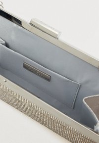 Strieborná kabelka s textúrovaným kovovým povrchom, saténovo podšitou vnútornou časťou, strieborným zatváraním a malou vreckom s embosovanou značkou.