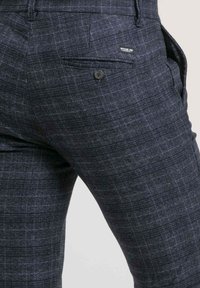 Pantalons à carreaux bleu marine en tissu texturé, dotés d'une poche arrière avec un bouton et d'un logo patch près de la taille.