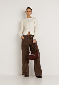 Gaiši bēša kardigana ar pogām, valkāta kopā ar augsta vidukļa, vaļīgām brūnām biksēm. Neliela bordo plecu soma papildina tēlu.