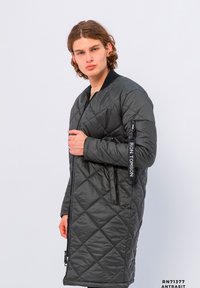 Gepolsterter schwarzer Daunenmantel mit Reißverschlusstaschen, geripptem Kragen und Logodetail am Ärmel, mit einem mittellangen Design und glatter Textur.