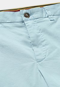 Světle modré bavlněné kalhoty s knoflíkovým zapínáním, poutky na opasek a jemným leskem. Uvnitř se objevují pruhované akcenty v červené a žluté barvě.