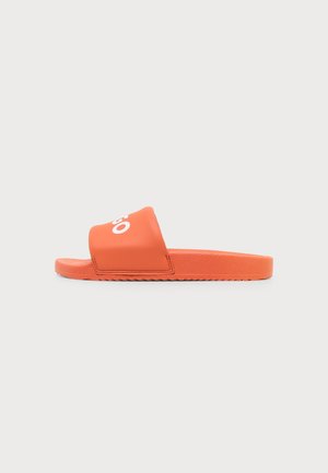Sandale slide orange avec une large bride comportant des inscriptions blanches, une semelle texturée et un design à bout ouvert plat sur un fond uni.