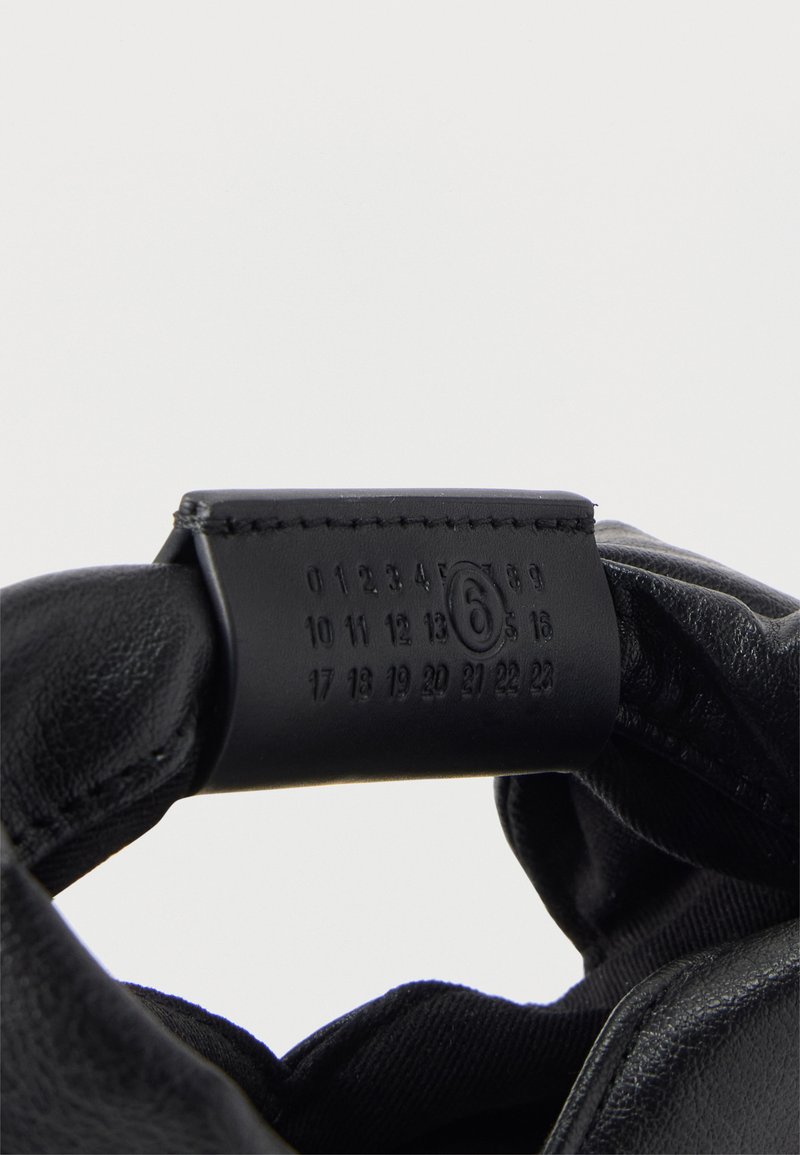 Gant en cuir noir tenu ouvert pour montrer une étiquette noire avec des chiffres en relief de 0 à 23, avec le chiffre 6 entouré.