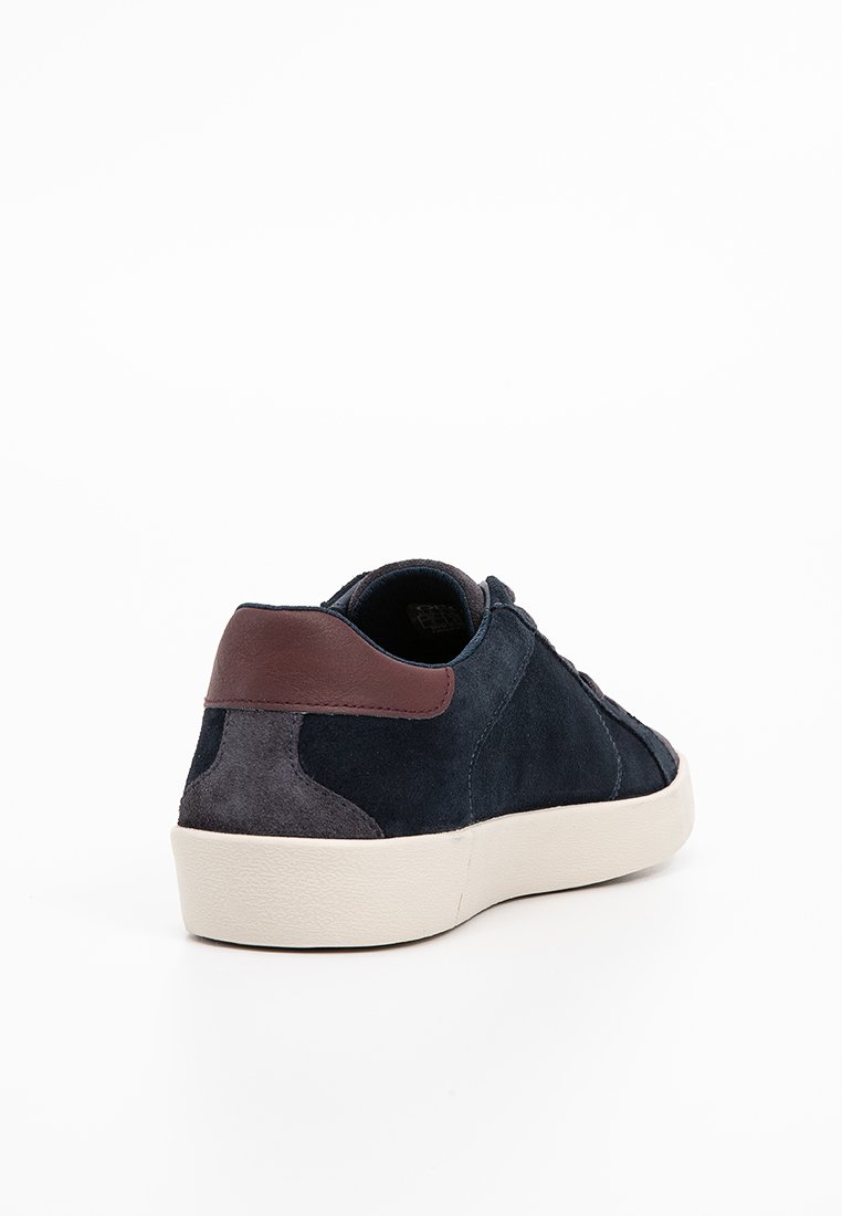 Baskets en suede bleu marine avec des accents de talons gris et marron, semelle blanche, vues de derrière sur un fond blanc.