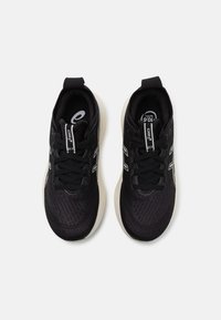 Baskets de sport noires avec un dessus texturé, un design à lacets, un col rembourré et une semelle intermédiaire blanche avec des détails de logo sur la languette.