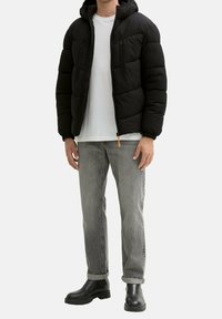 Musta toppatakki hupulla, jossa vetoketjulliset taskut, joustavat hihansuut ja kiristysnyöri helmassa. Yhdistetty harmaihin farkkuihin ja mustiin saappaisiin.