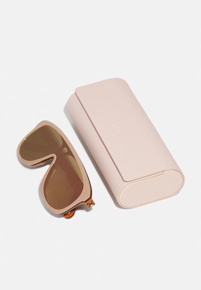Des lunettes de soleil avec une monture rose pâle et des verres teintés bruns, à côté d'une étui en cuir texturé assorti de couleur rose clair, de forme ovale.